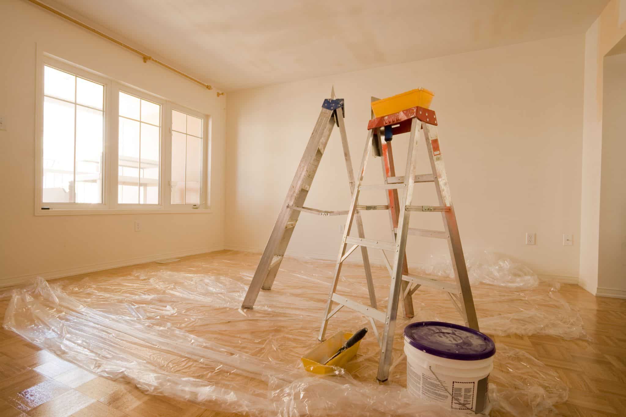 Modernes renoviertes Wohnzimmer mit großen Fenstern, hellem Holzfußboden, Malerleitern und Malerbedarf für professionelle Bausanierungen.