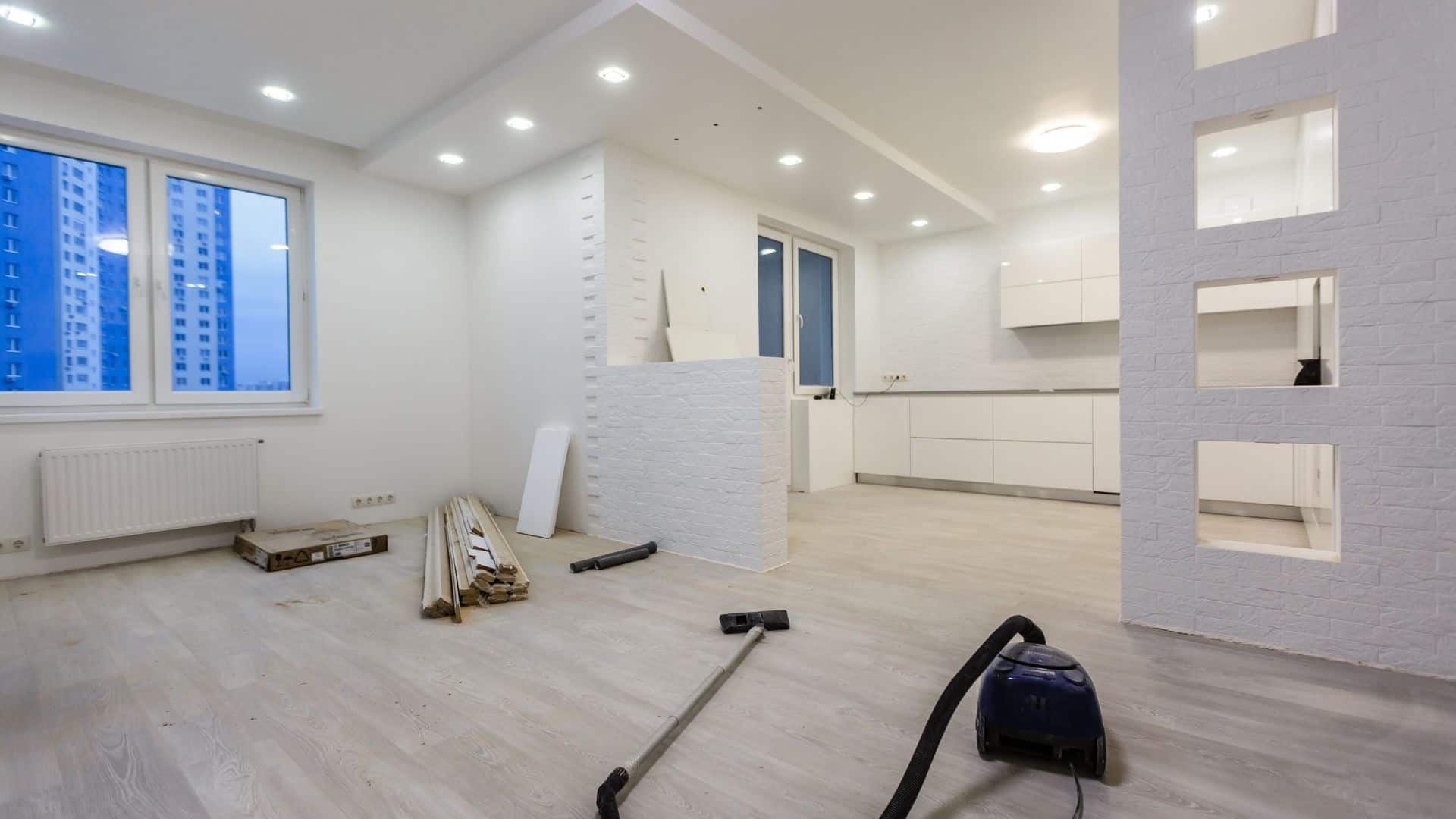 Moderne weiße Küchenrenovierung in neuem Apartment mit weißen Wänden und Holzfußboden, bereit für die Einrichtung, mit Blick auf eine Stadtansicht durch große Fenster.