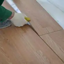Handwerker schneidet Laminatdiele passgenau zu, trägt Arbeitshandschuhe