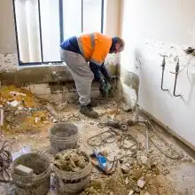 Handwerker führt Kernsanierung in Badezimmer durch, Bauschutt und Werkzeuge auf dem Boden